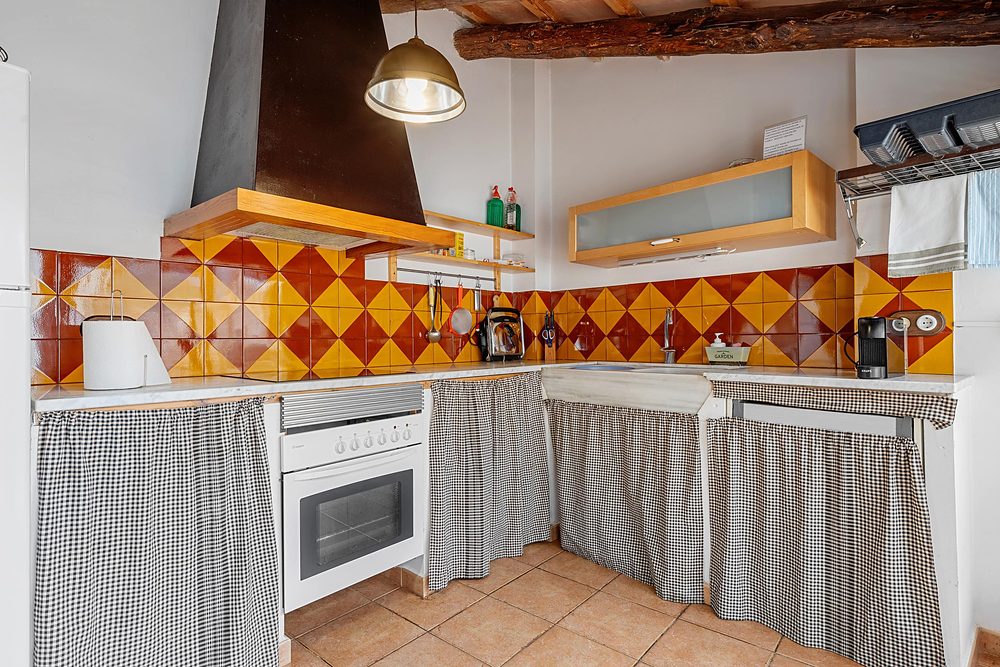 La cuina amb la rajola de rombes taronja i les cortines de quadres