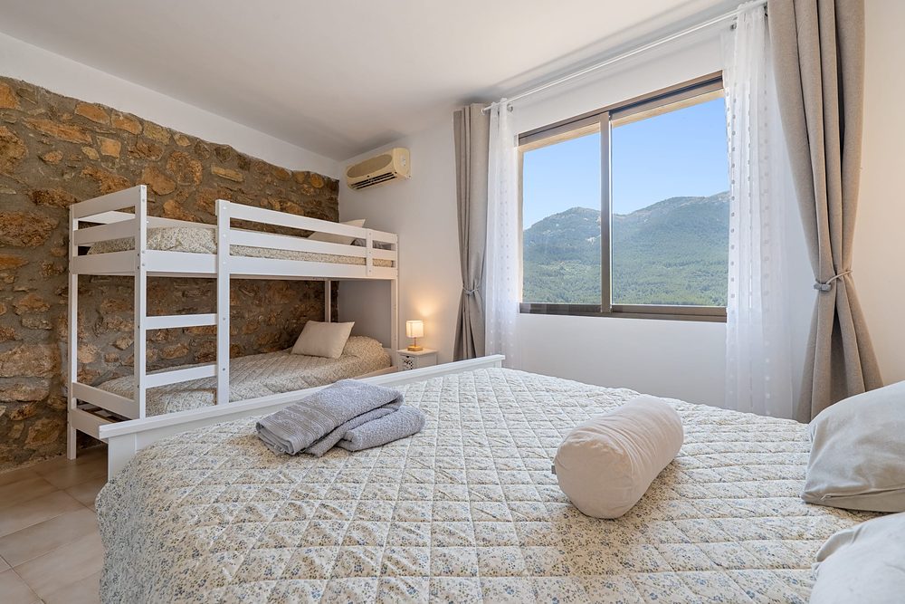 Dormitori amb paret de pedra, llit doble, llitera i vistes als Ports